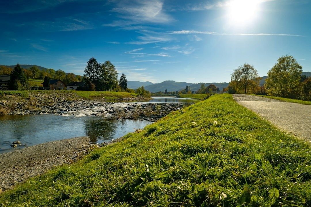 Renaturierter Fluss mit Radweg, Wiesen und bewaldeten Hügeln im Hintergrund